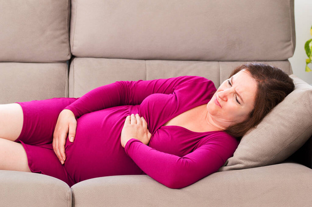 Shot of a pregnant woman suffering belly ache lying on a couch at home - Valokuva, kuva