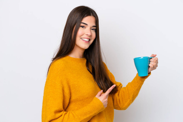 Young Brazilian woman holding cup of coffee isolated on white background and pointing it - Фото, изображение