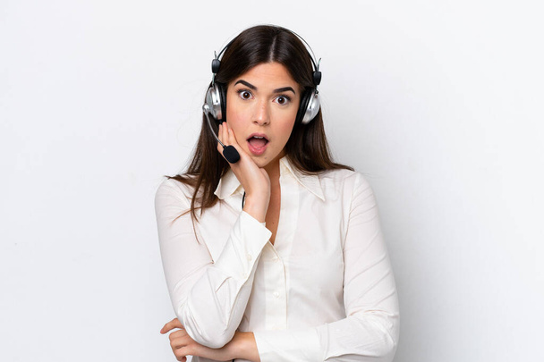 Telemarketer caucasian woman working with a headset isolated on white background surprised and shocked while looking right - Foto, imagen