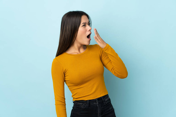 Teenager girl isolated on blue background yawning and covering wide open mouth with hand - Foto, imagen