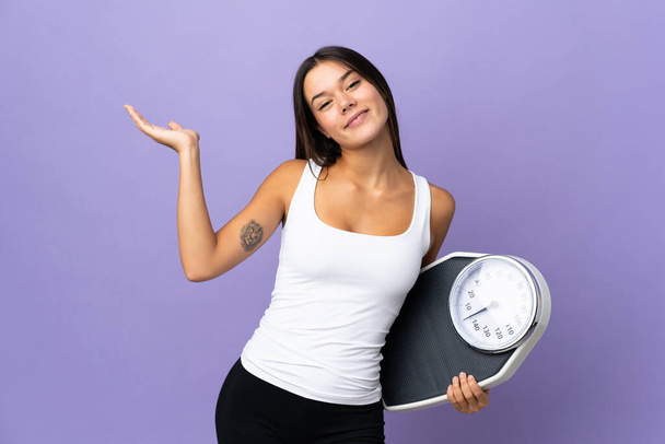 Teenager girl isolated on purple background with weighing machine - Photo, Image