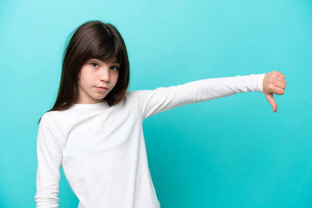 Little caucasian girl isolated on blue background showing thumb down with negative expression - Foto, Bild