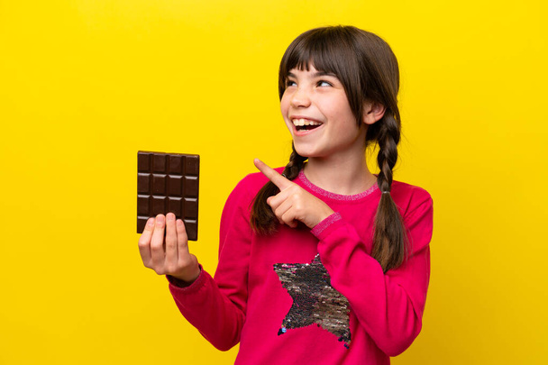 Little caucasian girl with chocolat isolated on yellow background intending to realizes the solution while lifting a finger up - Фото, зображення