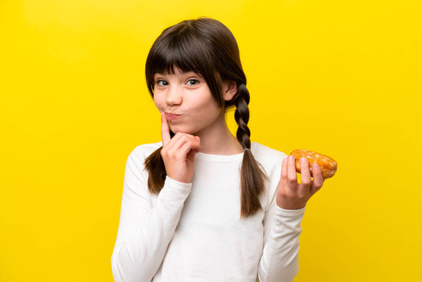 Little caucasian girl isolated on yellow background holding a donut - Foto, Imagen