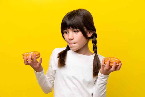 Little caucasian girl isolated on yellow background holding donuts - Фото, зображення