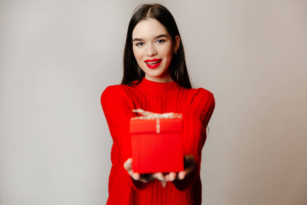 Attractive young woman with an appealing smile and romantic makeup. The girl is wearing a red sweater and has red lips - Photo, Image