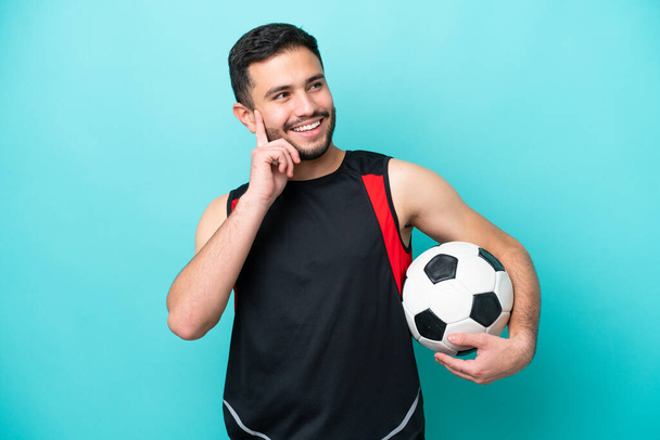 Genç futbolcu Brezilyalı adam mavi arka planda izole edilmiş bir şekilde yukarı bakarken bir fikir düşünüyor. - Fotoğraf, Görsel