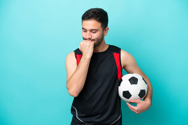 Молодой футболист бразилец изолирован на синем фоне с сомнениями - Фото, изображение