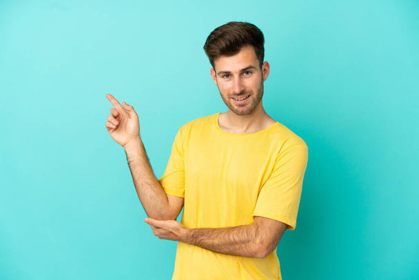 Young caucasian handsome man isolated on blue background happy and pointing up - Photo, Image