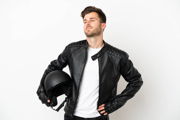 Молодий білий чоловік з мотоциклетним шоломом ізольований на білому тлі, позує руками на стегні і посміхається
 - Фото, зображення
