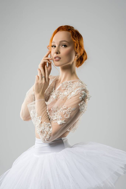 Alluring young ballerina in tutu touching face and looking at camera - Zdjęcie, obraz