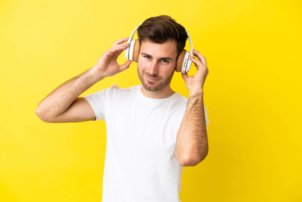 Sarı arka planda izole edilmiş beyaz yakışıklı bir adam müzik dinliyor. - Fotoğraf, Görsel