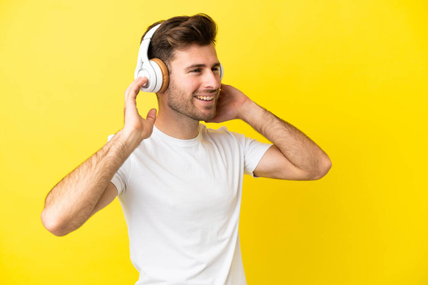Nuori valkoihoinen komea mies eristetty keltaisella taustalla kuuntelee musiikkia ja laulaa - Valokuva, kuva