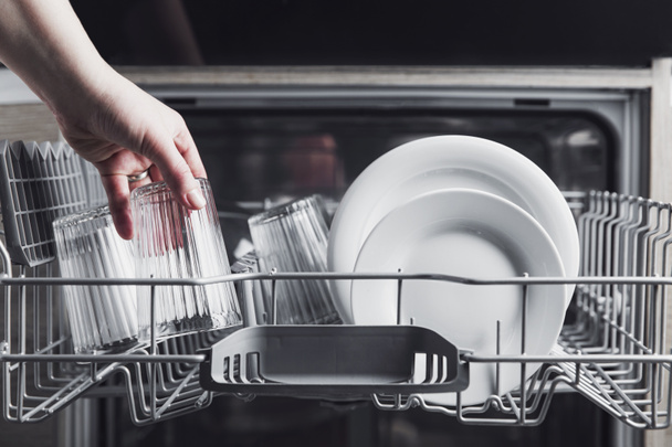 Відкрита посудомийна машина з чистими столовими приборами, окулярами, посудом всередині домашньої кухні
 - Фото, зображення