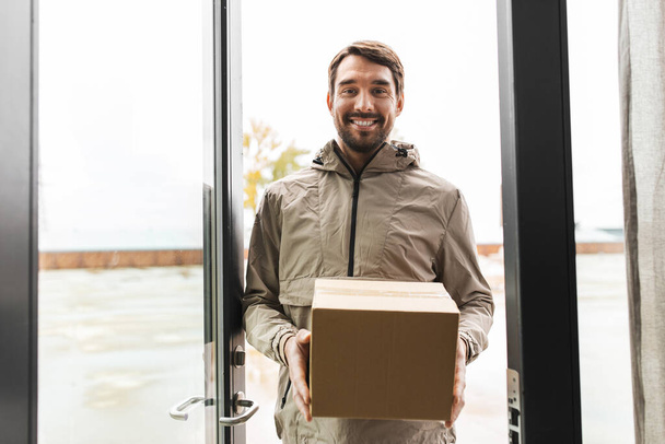 smiling delivery man with parcel box at open door - Foto, imagen
