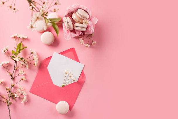 バレンタイン、誕生日、女性、母の日のための春祭りの休日の挨拶カード。ギフトボックスに甘いクッキーマカロンとピンクの背景に桜をバラ。トップビュー、コピースペース、フラットレイアウト. - 写真・画像