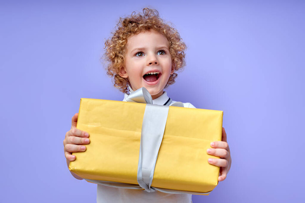 Excited child boy holding yellow gift box in hands, celebrating birthday - Foto, immagini