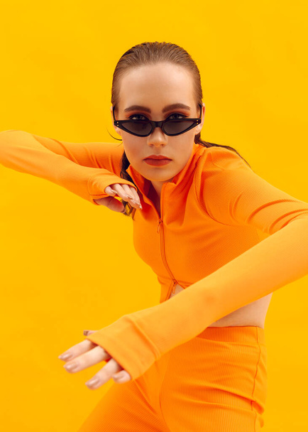 stylish girl in an orange suit on a yellow background in brown glasses - Foto, Imagem