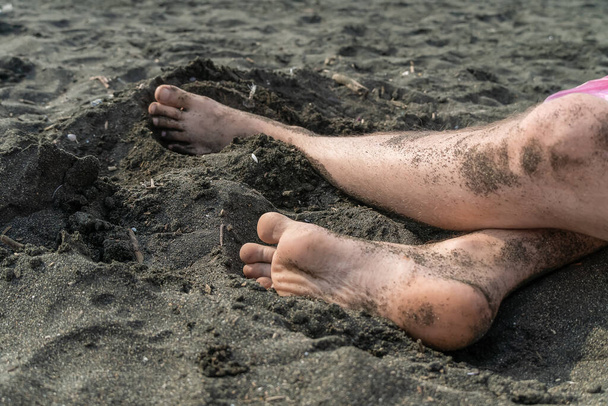 Κοντινό πλάνο των ποδιών των ανδρών σε μια αμμώδη παραλία με μαύρη άμμο - Φωτογραφία, εικόνα
