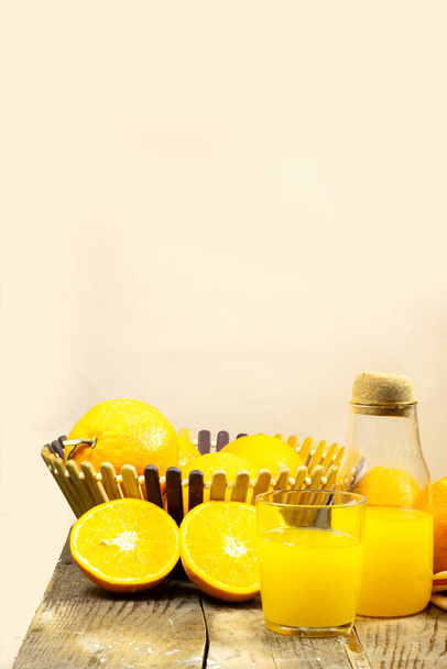 glass bottle of fresh orange juice with fresh fruits in basket on wooden planks table - Photo, Image