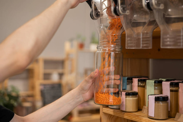A man fills a jar with red lentils. Selling bulk goods by weight in an eco store. Trade concept without plastic packaging - Foto, Bild