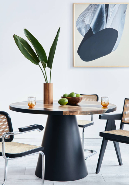 Stylish composition of dining room interior with design table, modern chairs, decoration, tropical leaf in vase, fruits, abstract mock up paintings and elegant accessories in home decor. Template. - Photo, Image