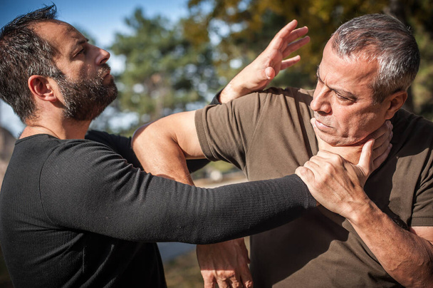 Kapap instructor demonstrates street fighting self defense technique against holds and grabs with his student - Foto, immagini
