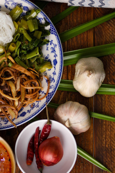 Macarrão de arroz tailandês com molho de amendoim servido em uma placa branca em uma mesa de madeira e decorado com folhas. - Foto, Imagem