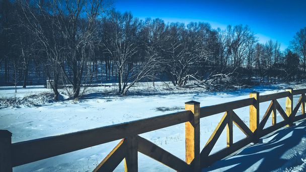 Houten omheining met bevroren rivier en bomen op de achtergrond - Foto, afbeelding