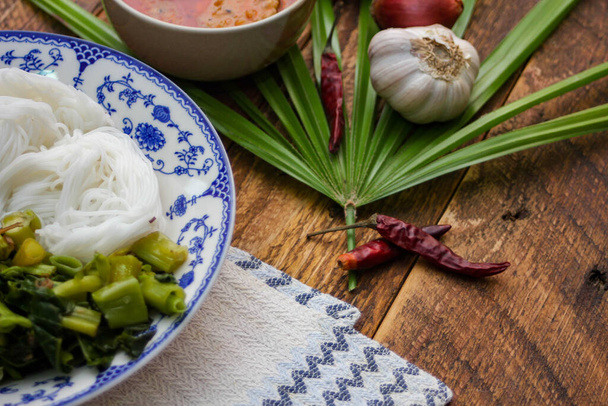 Thajská rýžová nudle s arašídovou omáčkou podávaná v bílém talíři na dřevěném stole a zdobená listy. - Fotografie, Obrázek