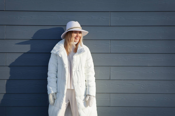 Authentic portrait of laughing blonde Woman on gray background with shadow from the sun, in winter warm white clothes looking away, happy face expression - Photo, Image