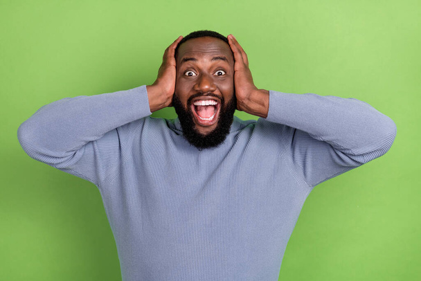Photo of impressed afro guy wear grey pullover open mouth arms head smiling isolated green color background - Photo, Image
