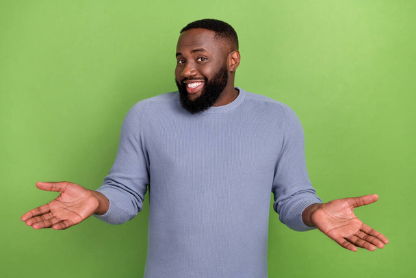 Photo of puzzled afro guy wear grey pullover shrugging shoulders smiling isolated green color background - Φωτογραφία, εικόνα