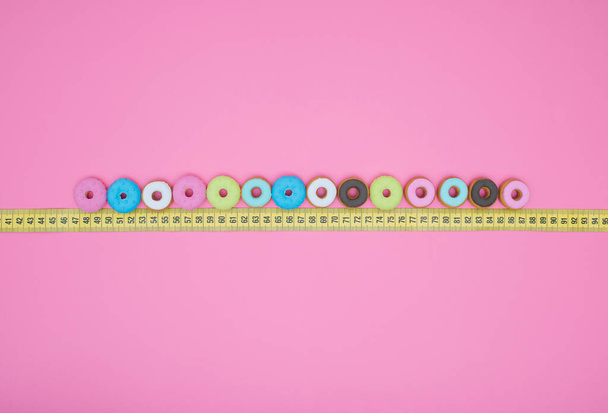 Keltainen mittanauha donitseilla pinkillä pastellitaustalla. Litteä pano. Hoikka käsite. - Valokuva, kuva