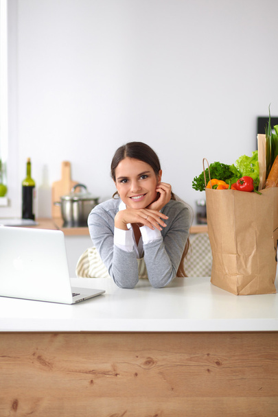Beautiful young woman cooking looking at laptop screen with receipt in the kitchen - Foto, Bild