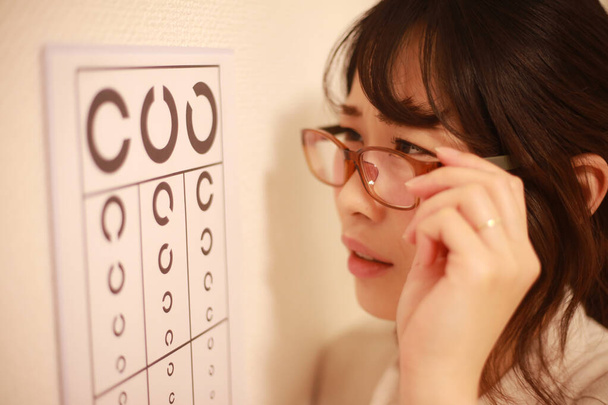 молодая азиатка в очках и с диаграммой теста на зрение - Фото, изображение