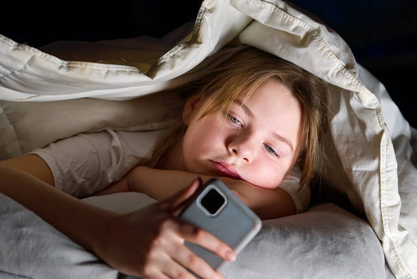 Geceleri battaniyenin altında cep telefonu olan bir kızın portresi. Gadget gecesi. Sosyal medya bağımlılığı. Siber zorbalık - Fotoğraf, Görsel