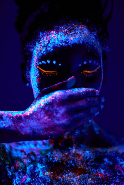 Абстрактный снимок красивой чернокожей женщины, закрывающей рот руками, с флюоресцентным боди-артом - Фото, изображение