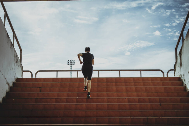 Una hermosa corredora corre por los escalones bajo la luz del sol. El concepto de entrar en el éxito, la auto-mejora en el ejercicio. - Foto, imagen