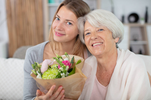 mother and daughter cuddling at home with flowers - Foto, Imagen