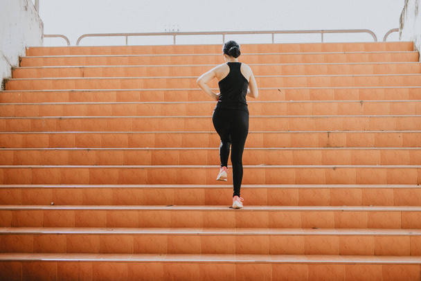 Eine schöne Läuferin joggt im Sonnenlicht die Stufen hinauf. Das Konzept des Erfolgs, der Selbstverbesserung in der Bewegung. - Foto, Bild