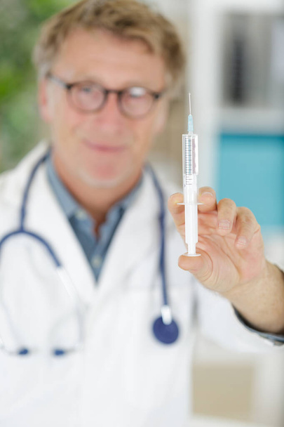 portrait of senior male doctor holding sterilized syringe - Фото, изображение