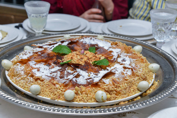 Inyección de comida de un tamaño familiar crujiente deliciosa pastilla marroquí gourmet en un plato de adornos cubierto con azúcar glaseado y canela en un mantel de lino con gafas, cuchillo, tenedor y servilletas
 - Foto, imagen