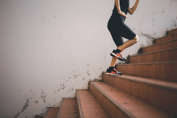 Μια όμορφη δρομέας γυναίκα τρέχει μέχρι τα σκαλιά κάτω από το φως του ήλιου. Η έννοια του βήματος προς την επιτυχία, αυτοβελτίωση στην άσκηση. - Φωτογραφία, εικόνα