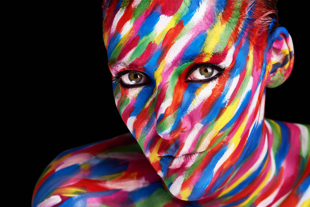 Live life vividly. Studio shot of a young woman posing with brightly colored paint on her face against a black background. - Foto, afbeelding