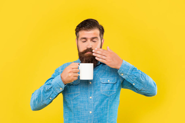 Serious caucasian man with closed eyes smelling coffee holding hot cup yellow background - Fotoğraf, Görsel
