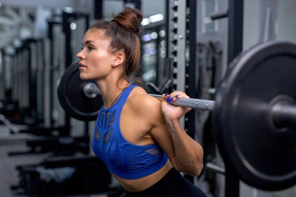 muscular woman training with heavy barbell for pulling, squatting, fitness in gym. - Foto, Imagem