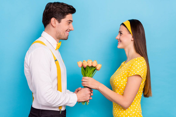 Profile photo of handsome guy attractive lady hold fresh tulips look each other isolated on blue color background - Foto, Imagem