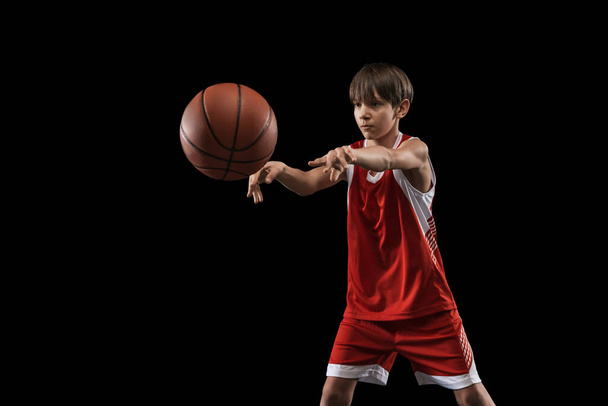 Cropped portrait of teen boy playing basketball isolated over black background - Фото, изображение