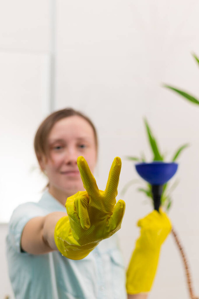 Une jeune femme de ménage en gants de caoutchouc hygiénique jaune dans une salle de bain lumineuse avec un piston pour nettoyer le blocage dans ses mains. Concentration sélective. Portrait - Photo, image